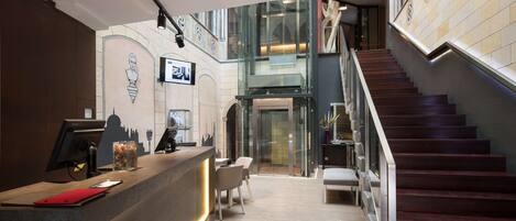 A modern reception area with a desk, chairs, and a staircase.