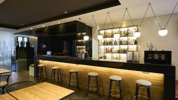 Zona de bar moderna con taburetes de madera, una barra con una exhibición de botellas e iluminación colgante.