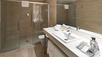 A modern bathroom with a glass-enclosed shower, a large mirror, and a white vanity with toiletries.
