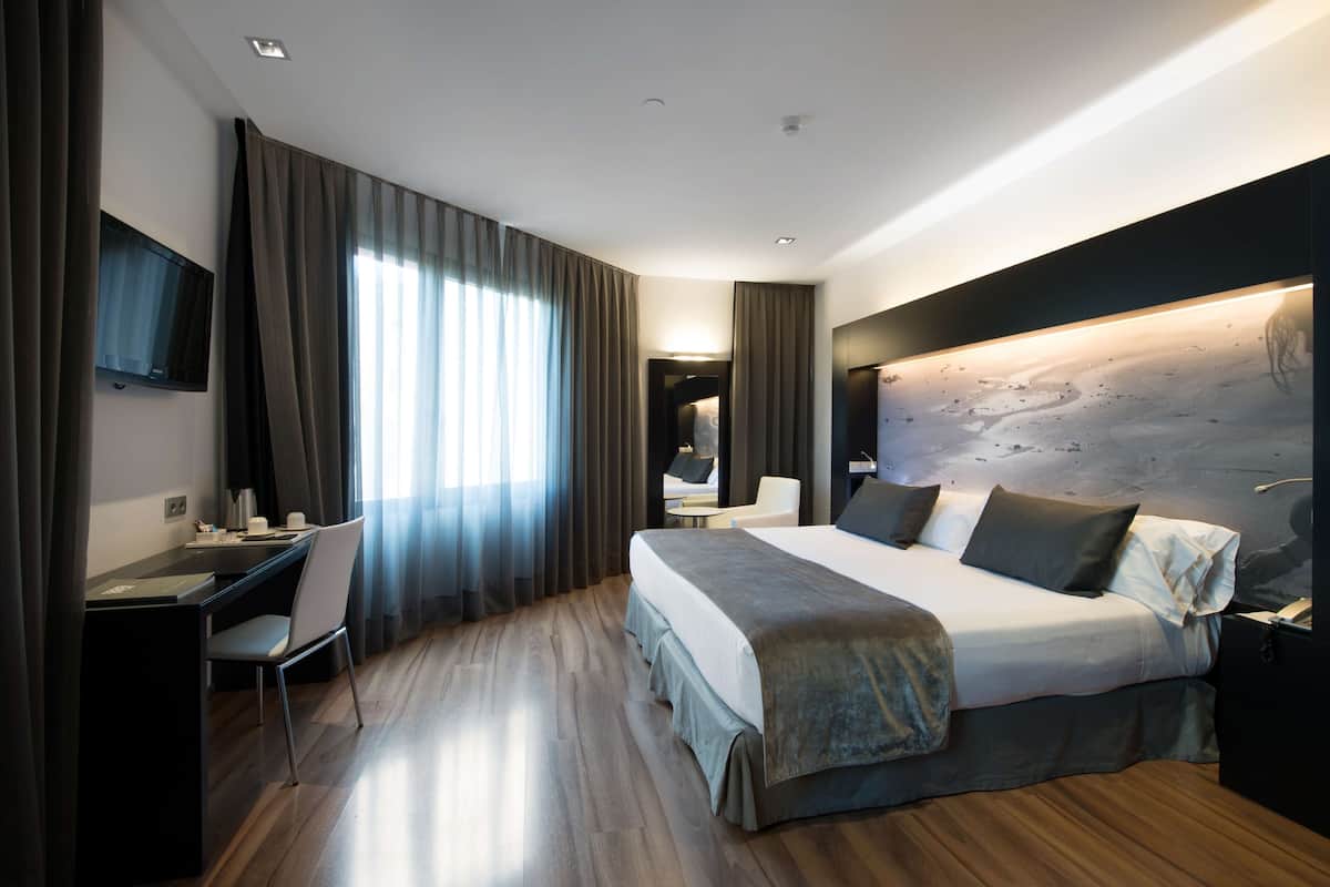 Moderni hotellihuone, jossa on suuri sänky, työpöytä ja tuoli.