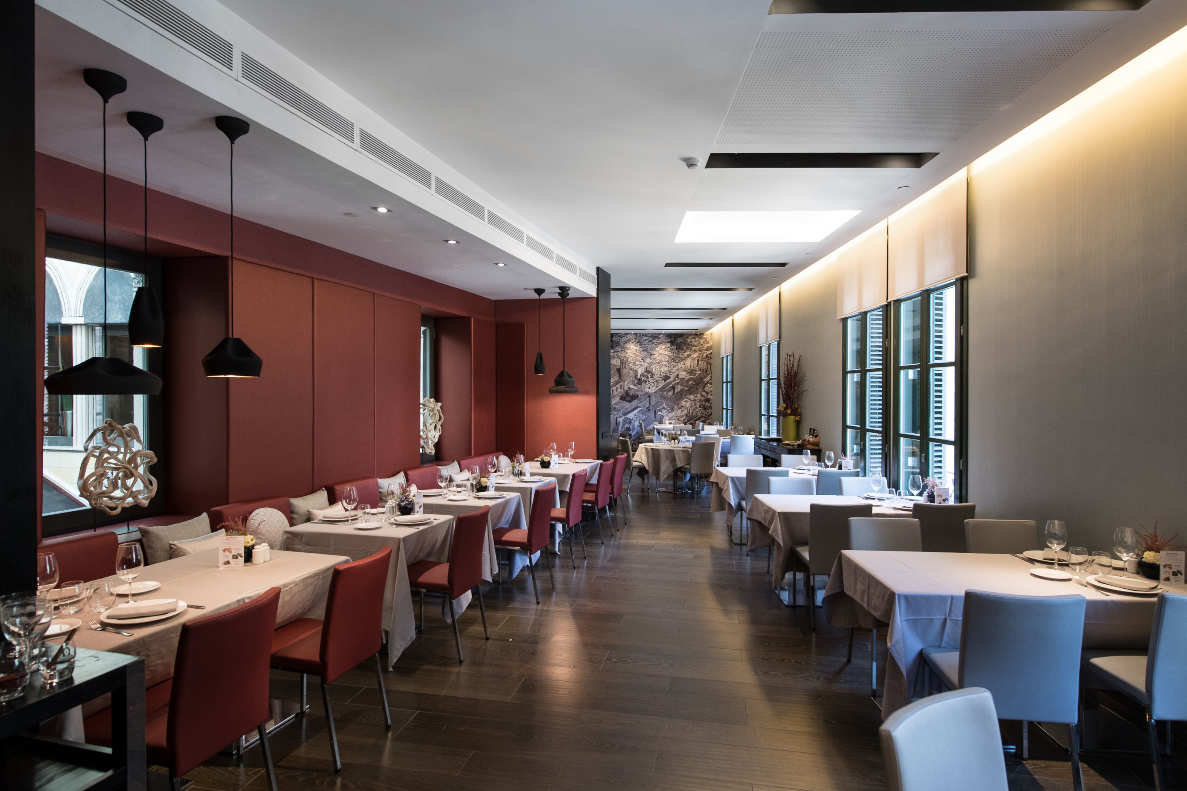Ein modernes Restaurant mit langen Tischen und Stühlen, Holzboden und Pendelleuchten.