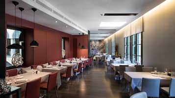 A modern restaurant with long tables and chairs, a wooden floor, and pendant lighting.