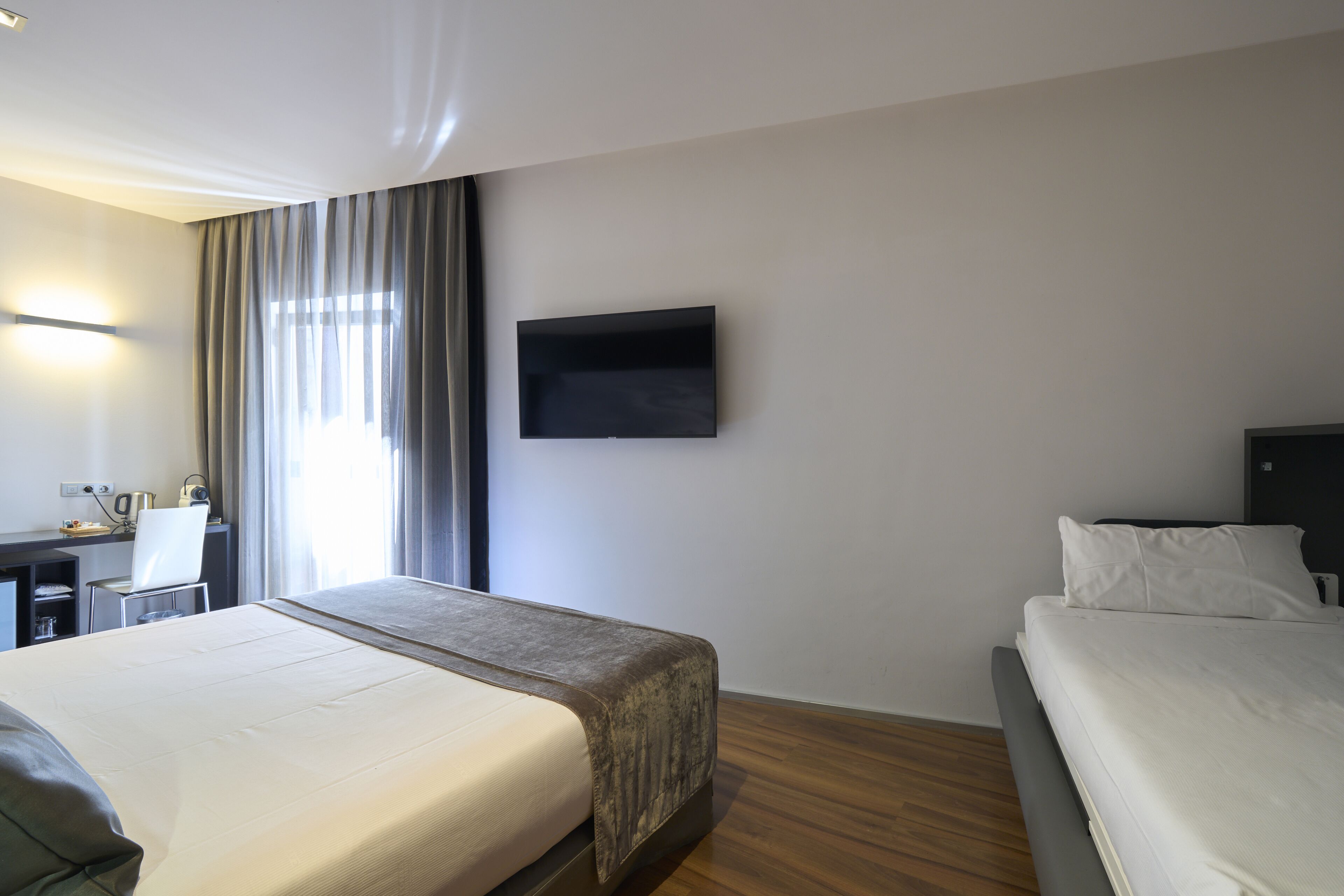A hotel room with a large bed, a desk, a chair, a television, and a window with curtains.