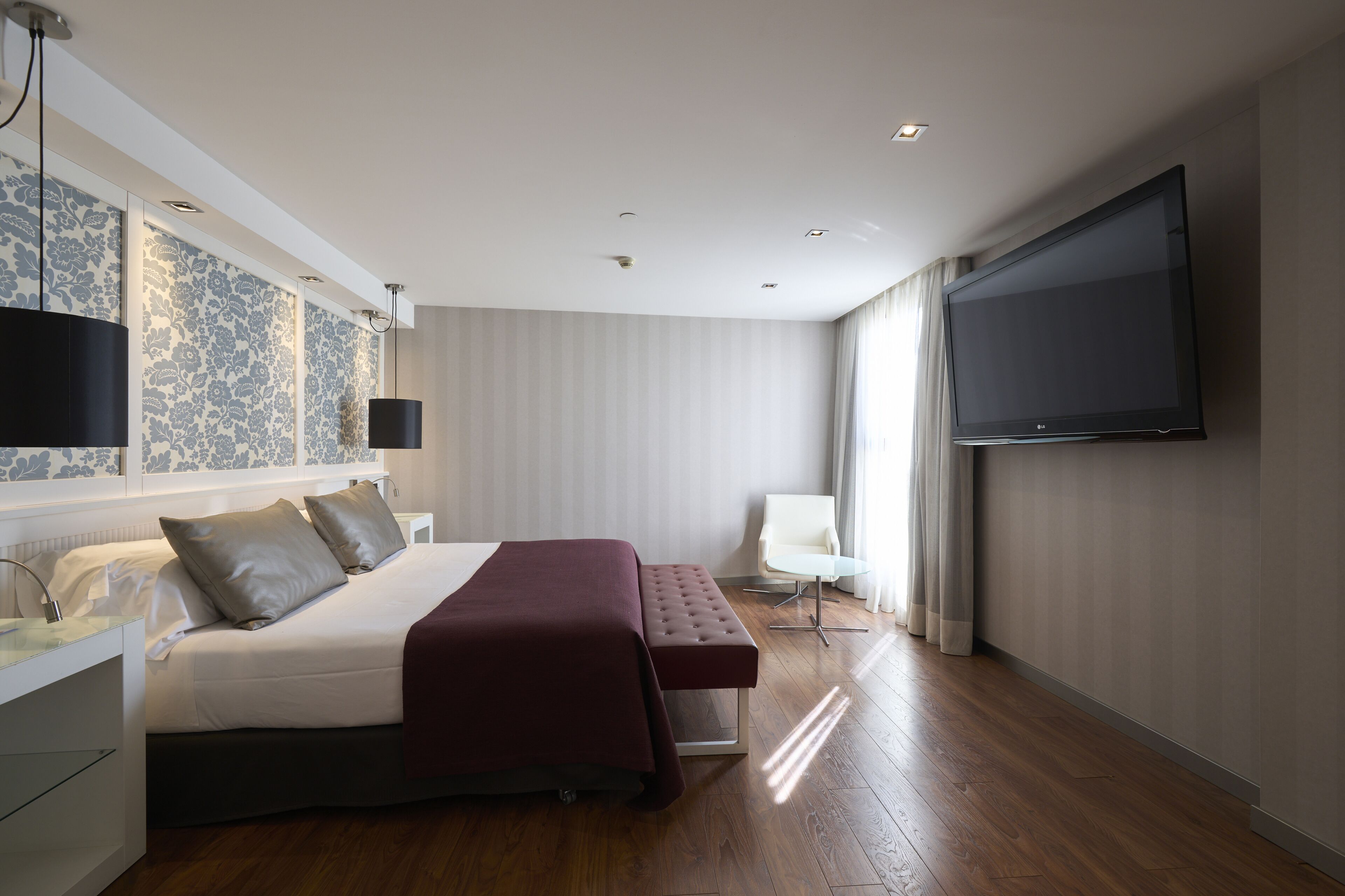 Una habitación de hotel moderna con una cama grande, un televisor de pantalla plana, una mesita de noche y una silla.