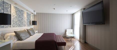 Una habitación de hotel moderna con una cama grande, un televisor de pantalla plana, una mesita de noche y una silla.