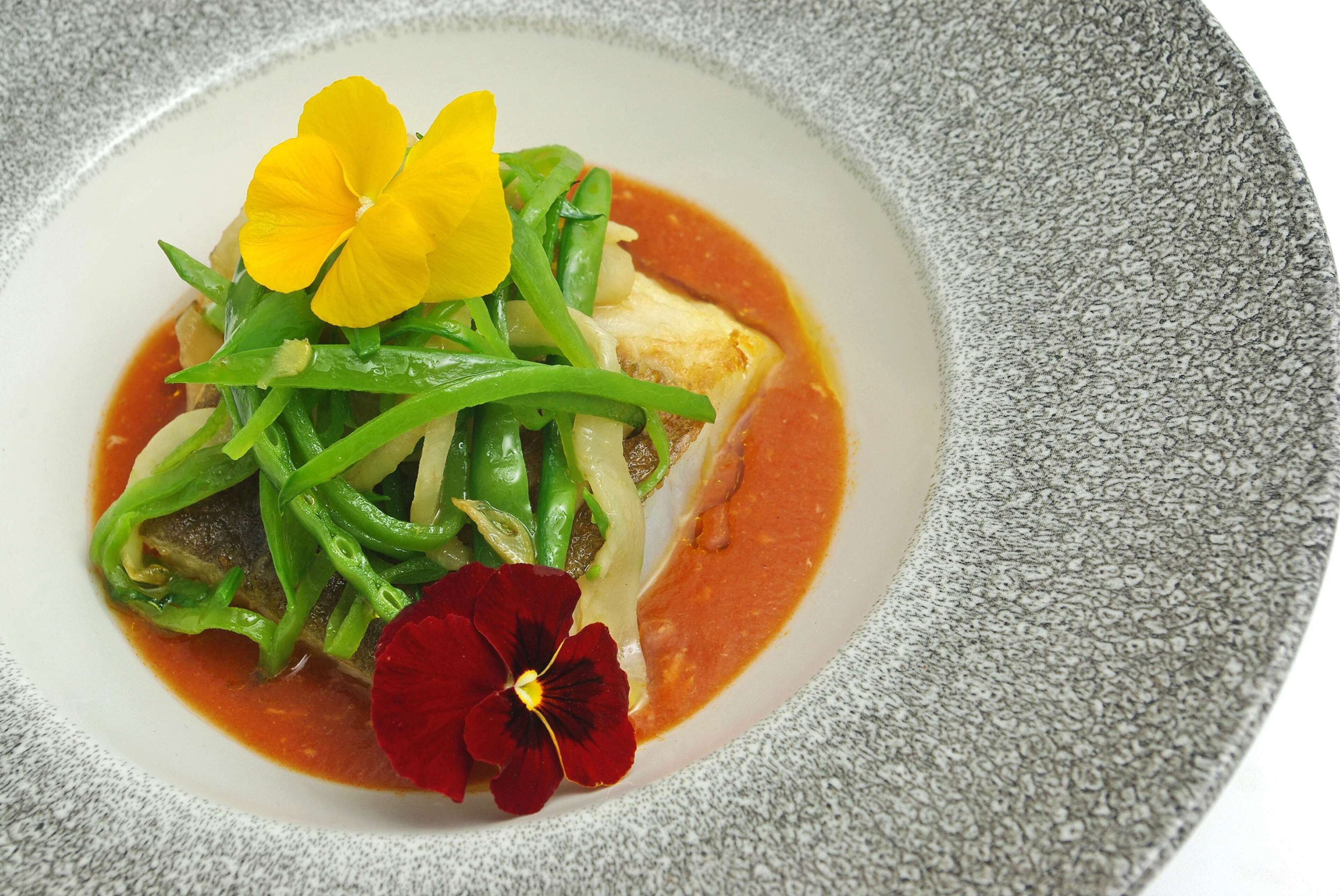 A dish with green vegetables and flowers on a white plate.