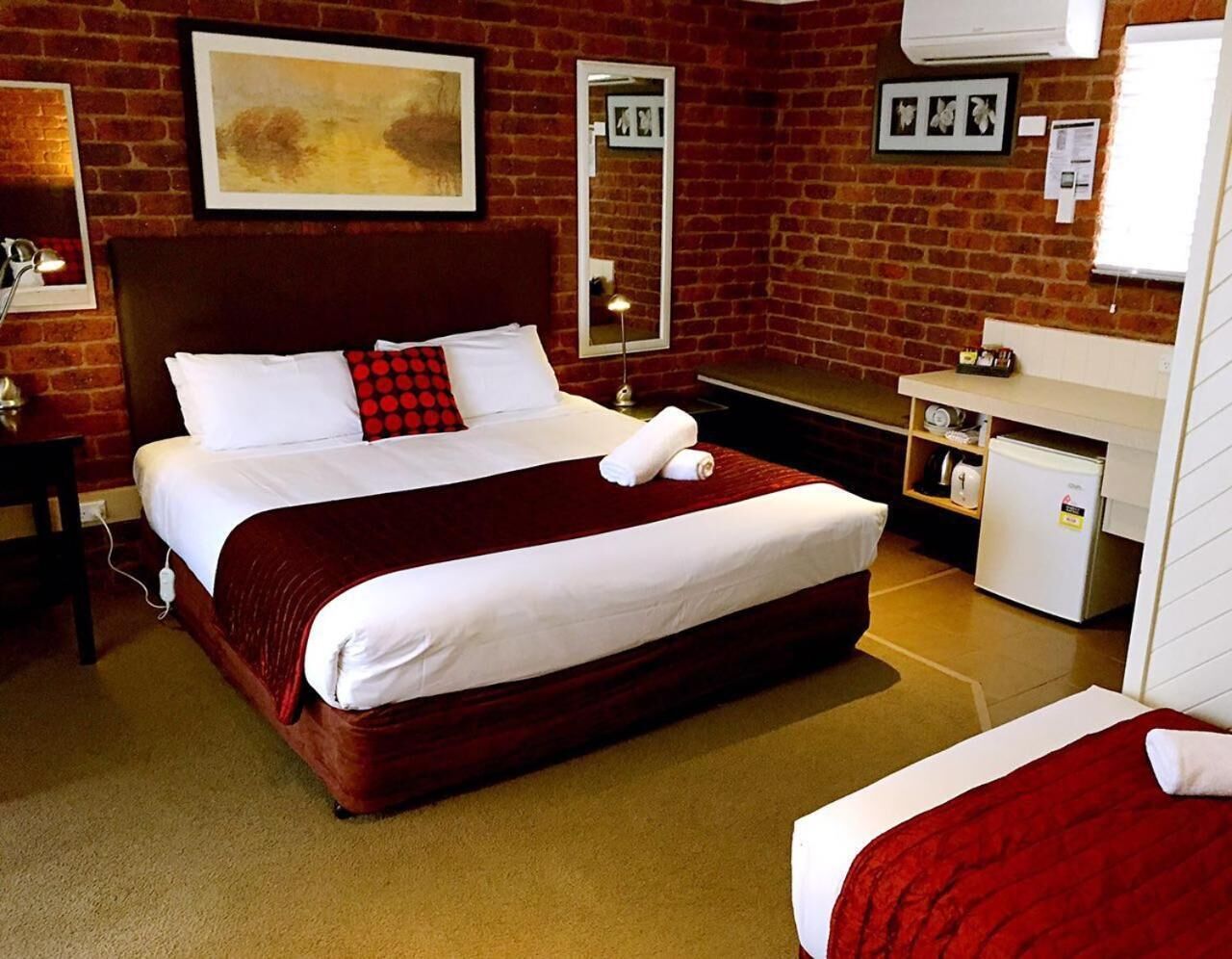 Habitación de hotel con una cama grande, un escritorio pequeño, un refrigerador y una pared de ladrillo.