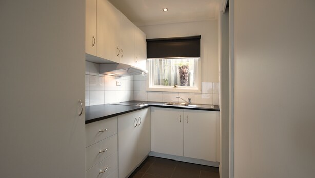 A modern kitchen with white cabinets, a black countertop, and a window with a view of greenery. - Admiral Motor Inn (Rosebud)