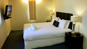 A hotel room with a large bed, two bedside tables, a TV mounted on the wall, and a window with curtains. - Admiral Motor Inn (Rosebud)