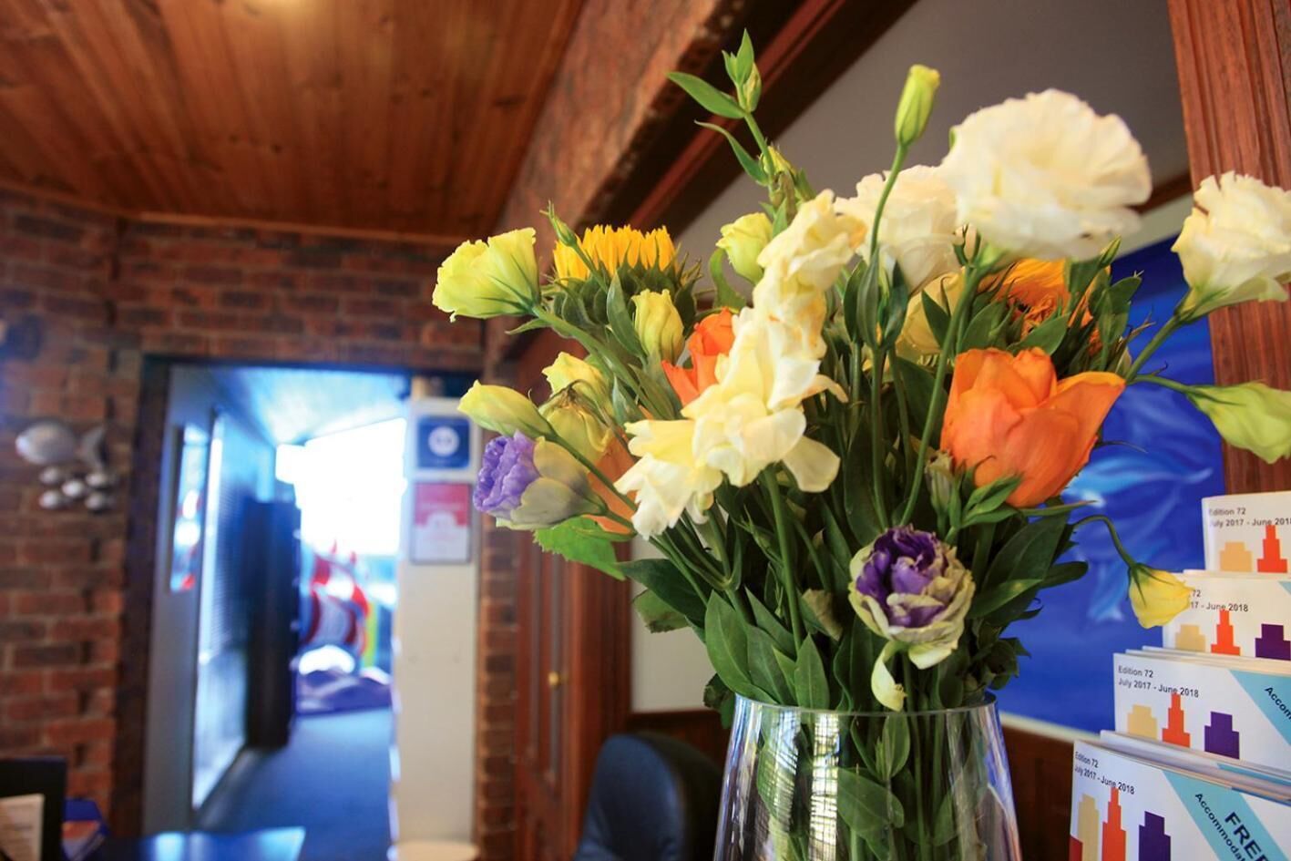 A bouquet of flowers in a clear vase on a table in a room with brick walls and wooden beams.