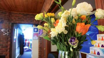 A bouquet of flowers in a clear vase on a table in a room with brick walls and wooden beams.