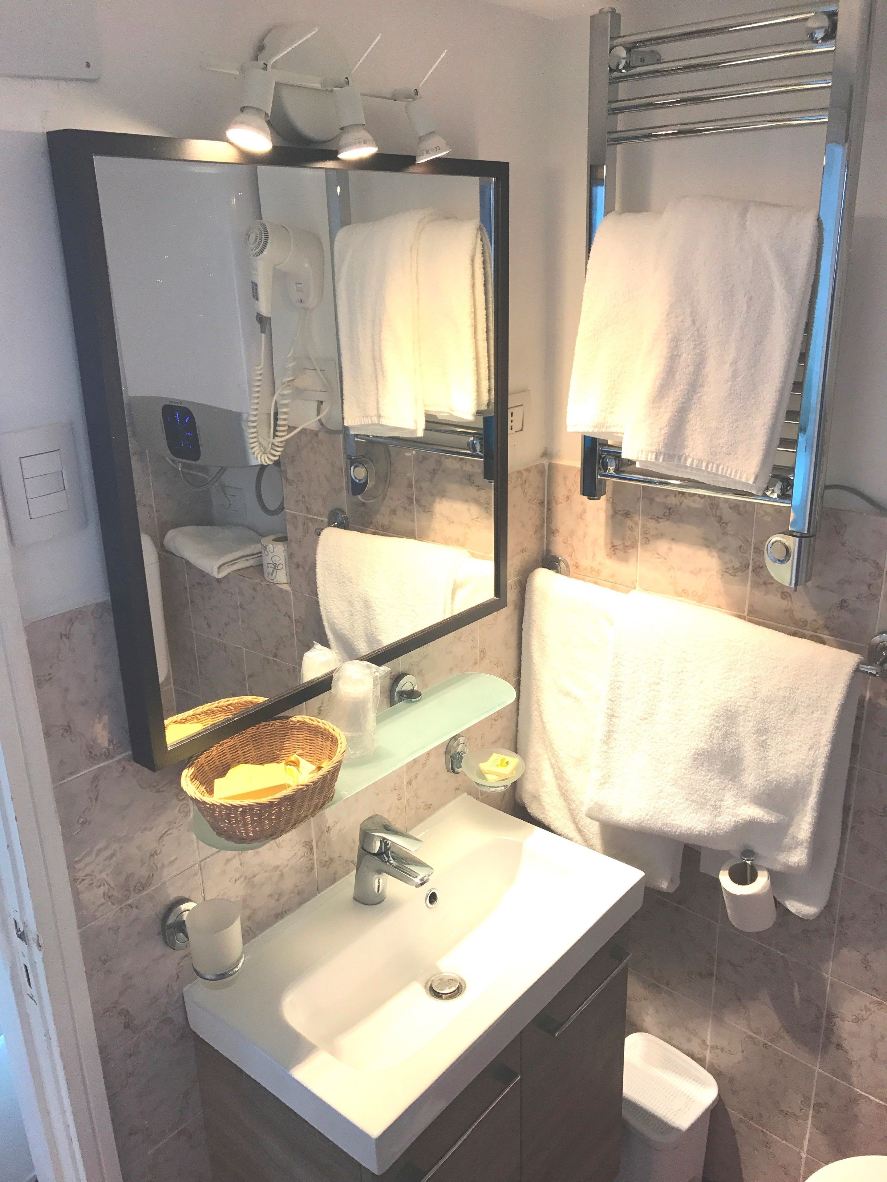Un baño con lavamanos blanco, espejo, toallero y zona de ducha.