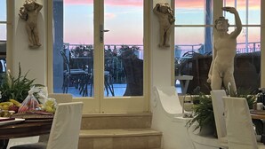 A room with a view of the sunset through large windows, featuring a statue on the wall and a staircase leading to an outdoor area. - Hotel La Reginella  (Capri)