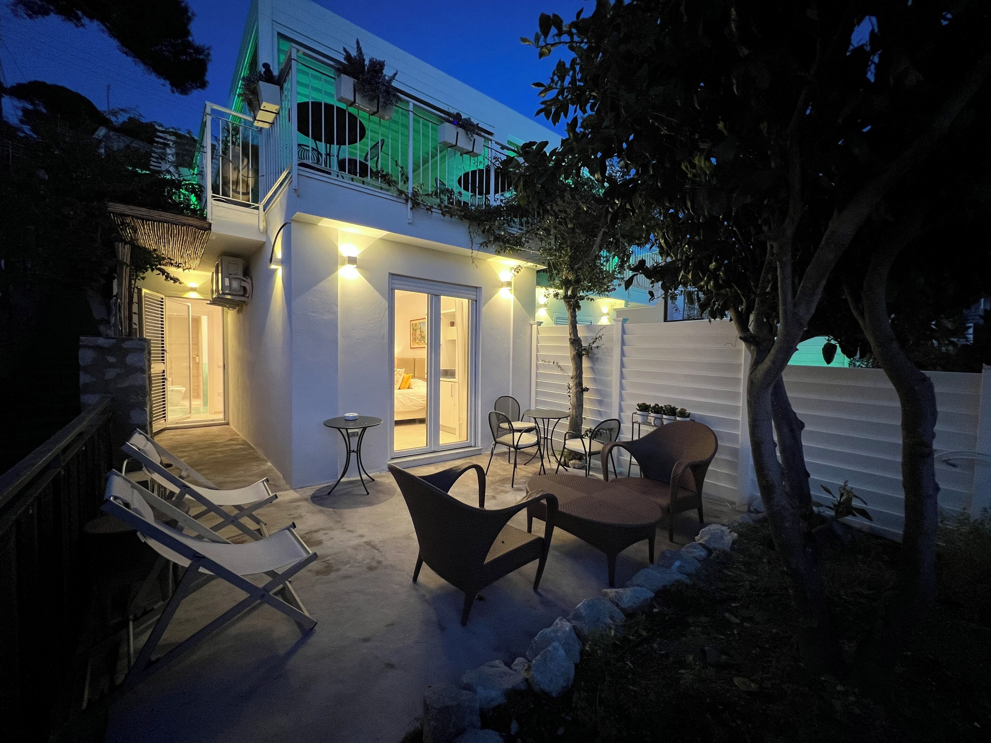 A modern building with a balcony, outdoor seating area, and a well-lit entrance.