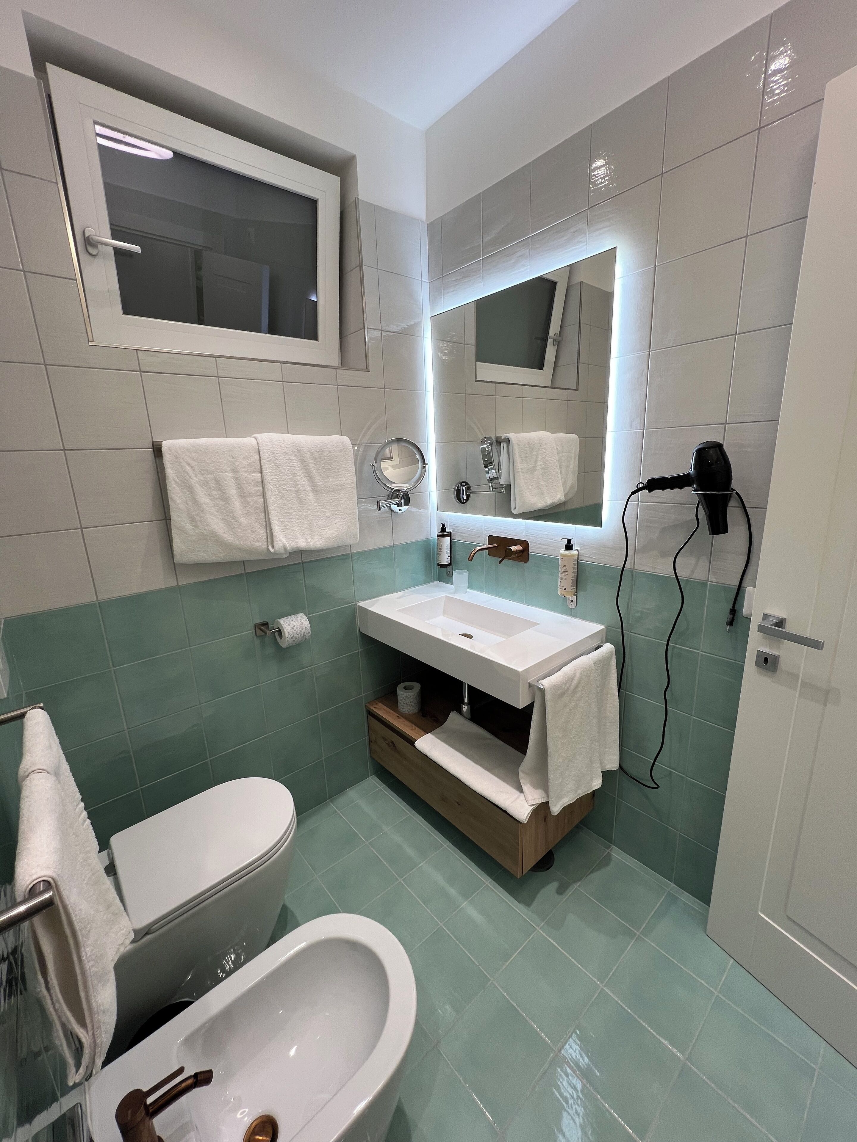 A bathroom with a white toilet, a sink with a mirror above it, and a hairdryer on the wall.