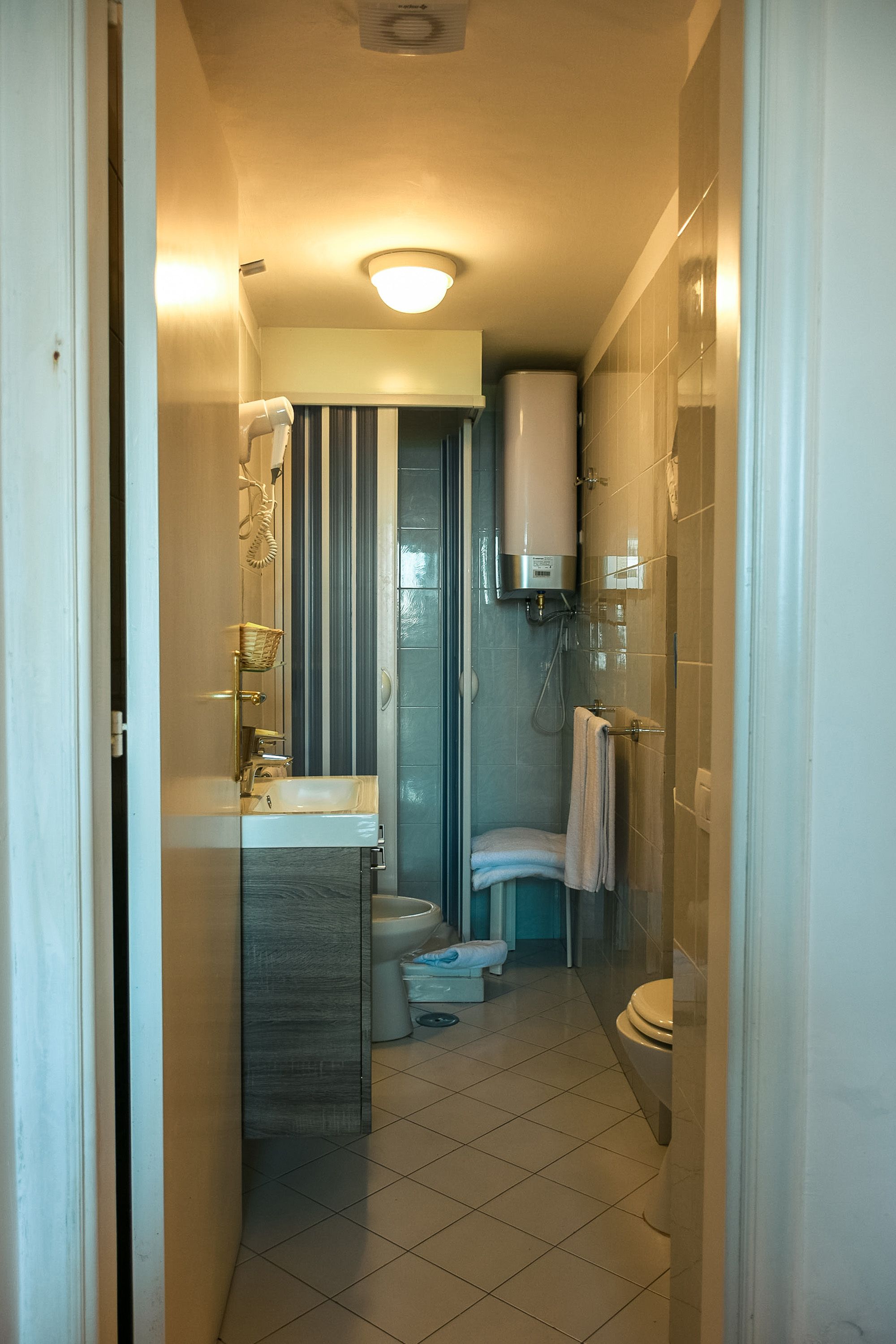 A narrow bathroom with a toilet, sink, and shower area.