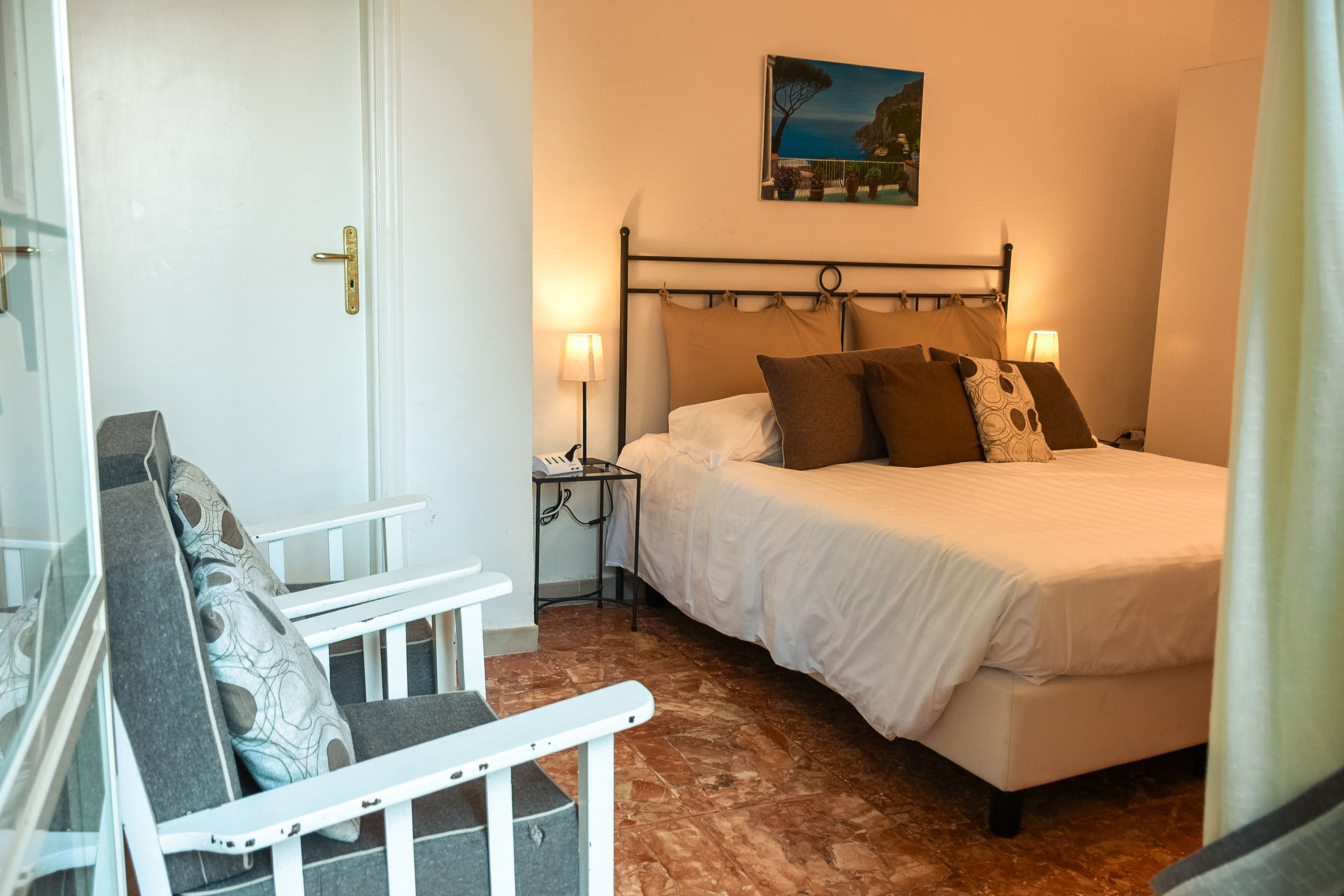 A bedroom with a bed, bedside tables, a chair, and a painting on the wall.