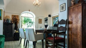 A dining area with a chandelier, a wooden chair with a red cushion, a green sofa, and a cabinet. - Hotel La Reginella  (Capri)