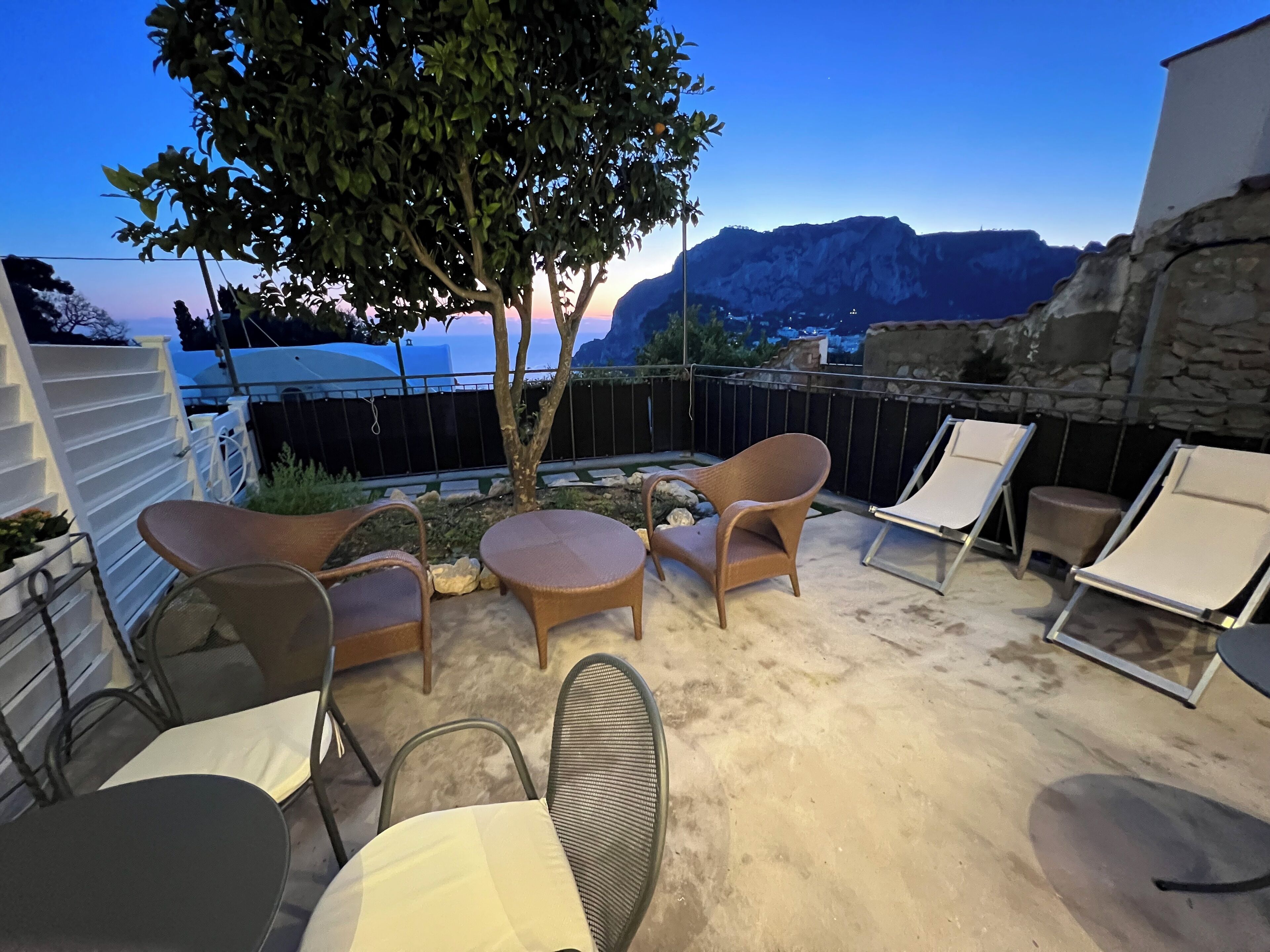 Un patio con mobiliario exterior, un árbol y vistas a montañas.