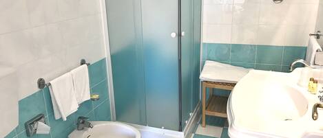 A bathroom with a bidet, a sink, and a shower stall.