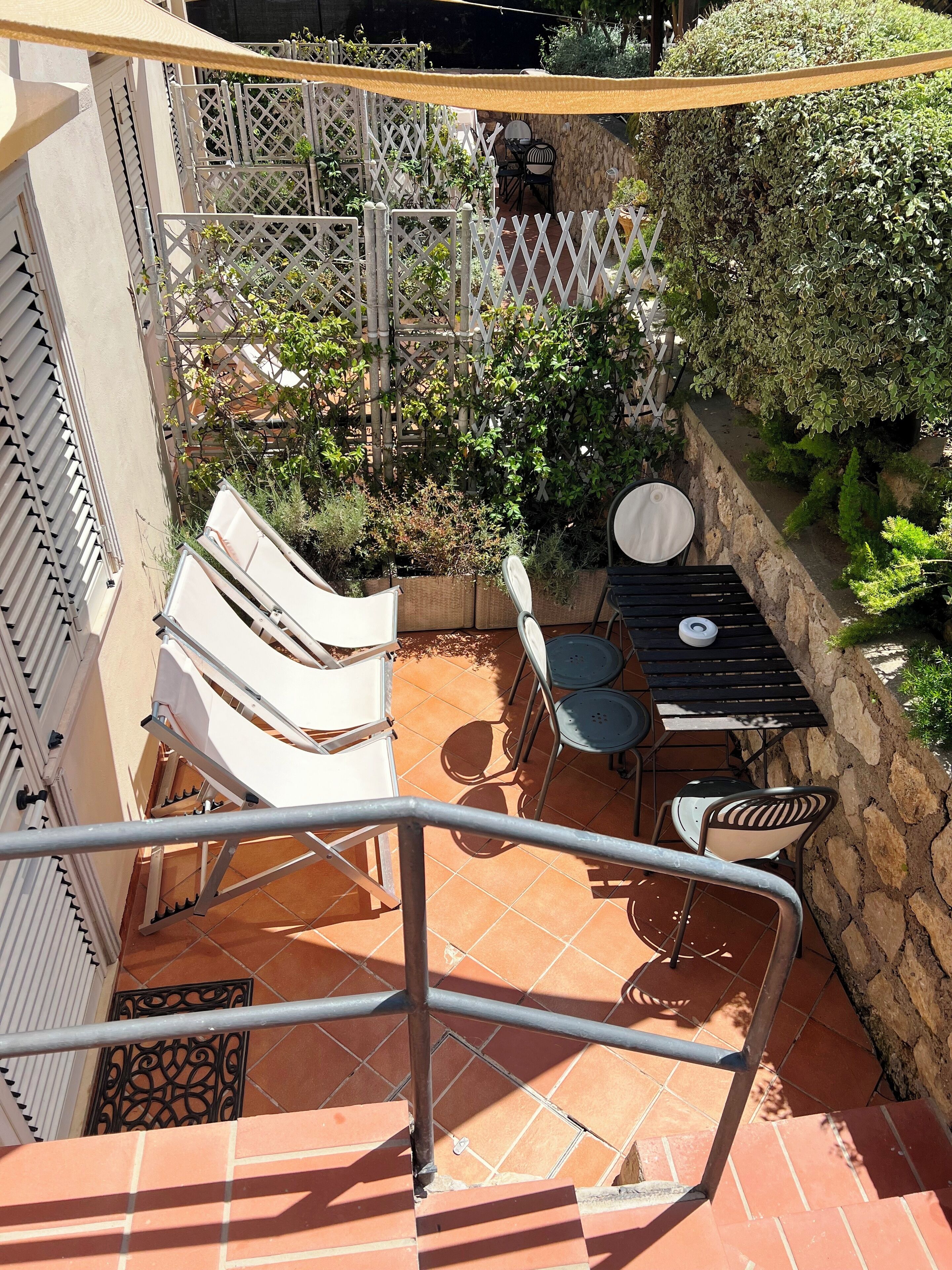 Ein Patio mit einer Sitzecke inklusive Stühle und Tisch, umgeben von einem weißen Gitterzaun und Pflanzen.