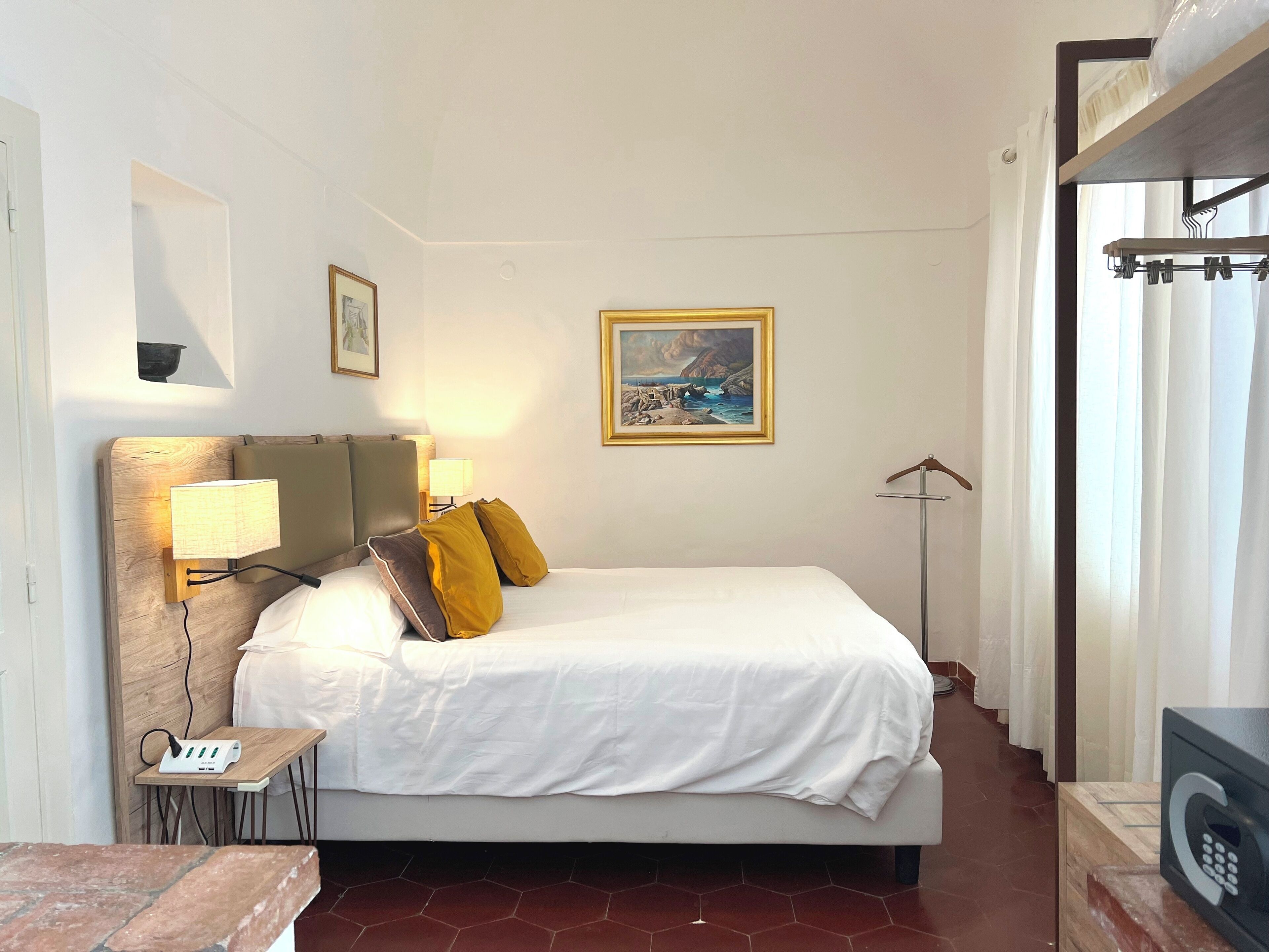 Une chambre d’hôtel avec un lit, une table de chevet avec une lampe, un tableau au mur et un porte-manteau.
