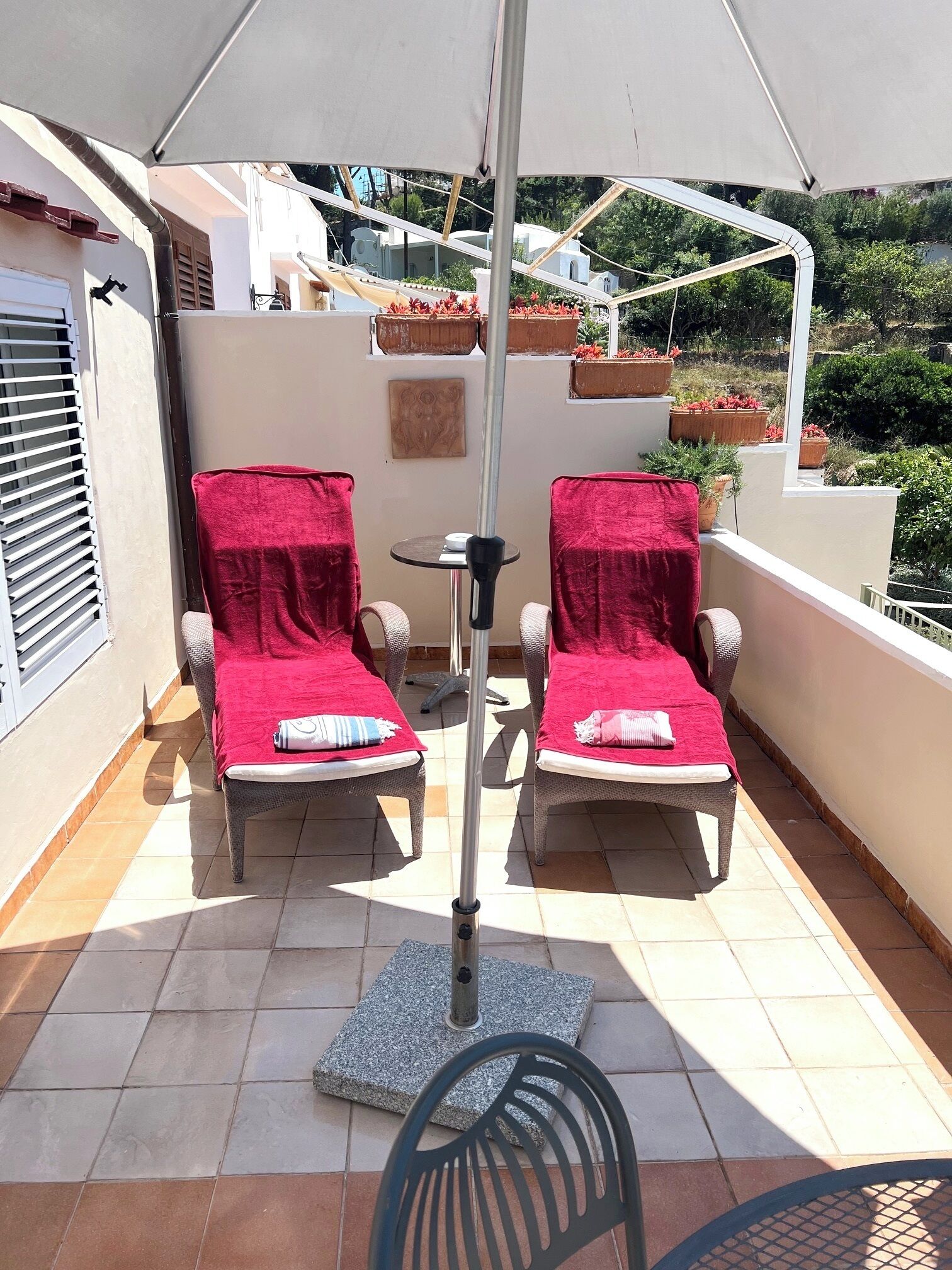 A balcony with two wicker lounge chairs covered with red towels, a small round table, and a metal pole.