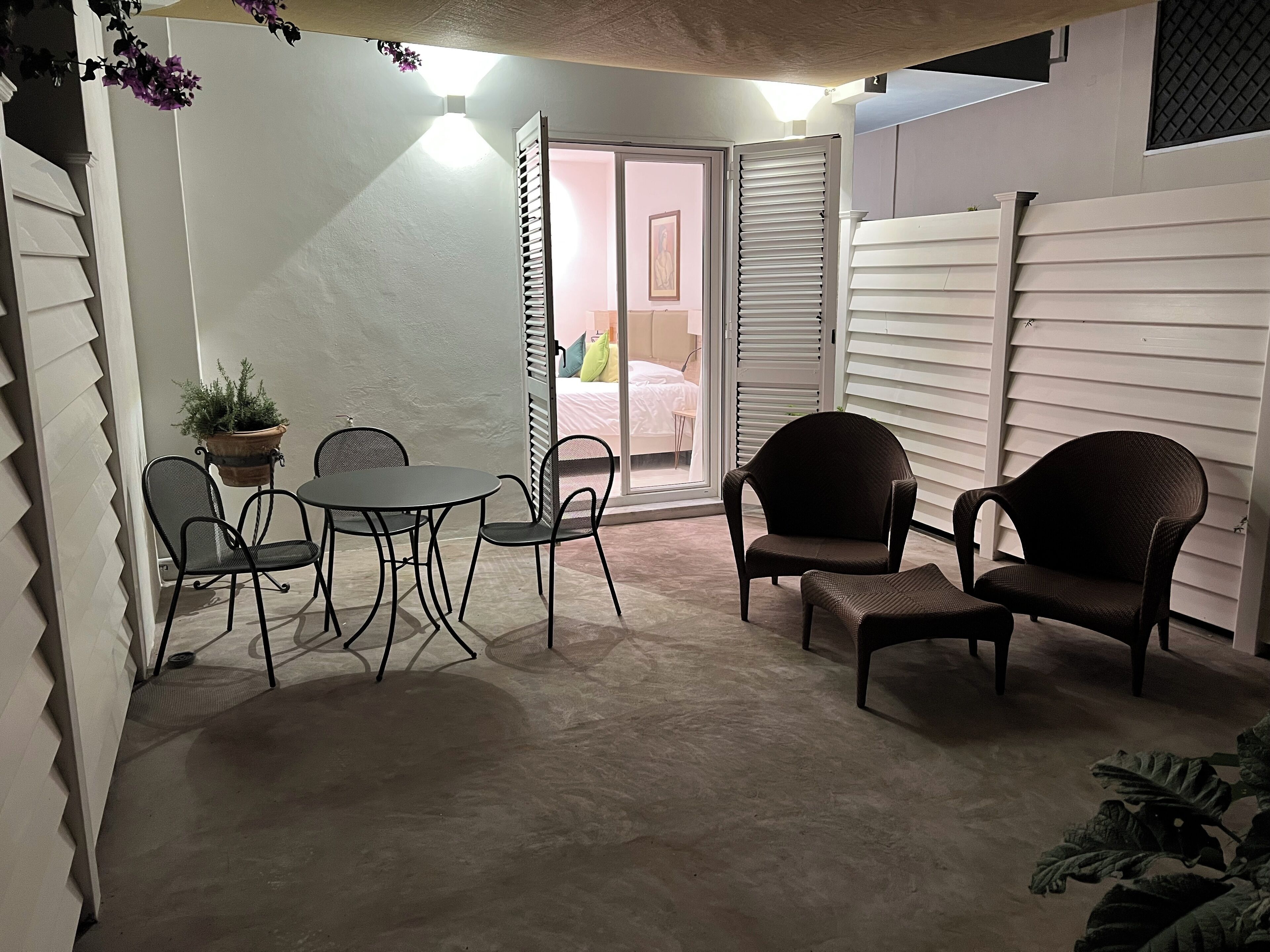A patio area with a round table and chairs, a potted plant, and a sliding glass door leading to a bedroom.
