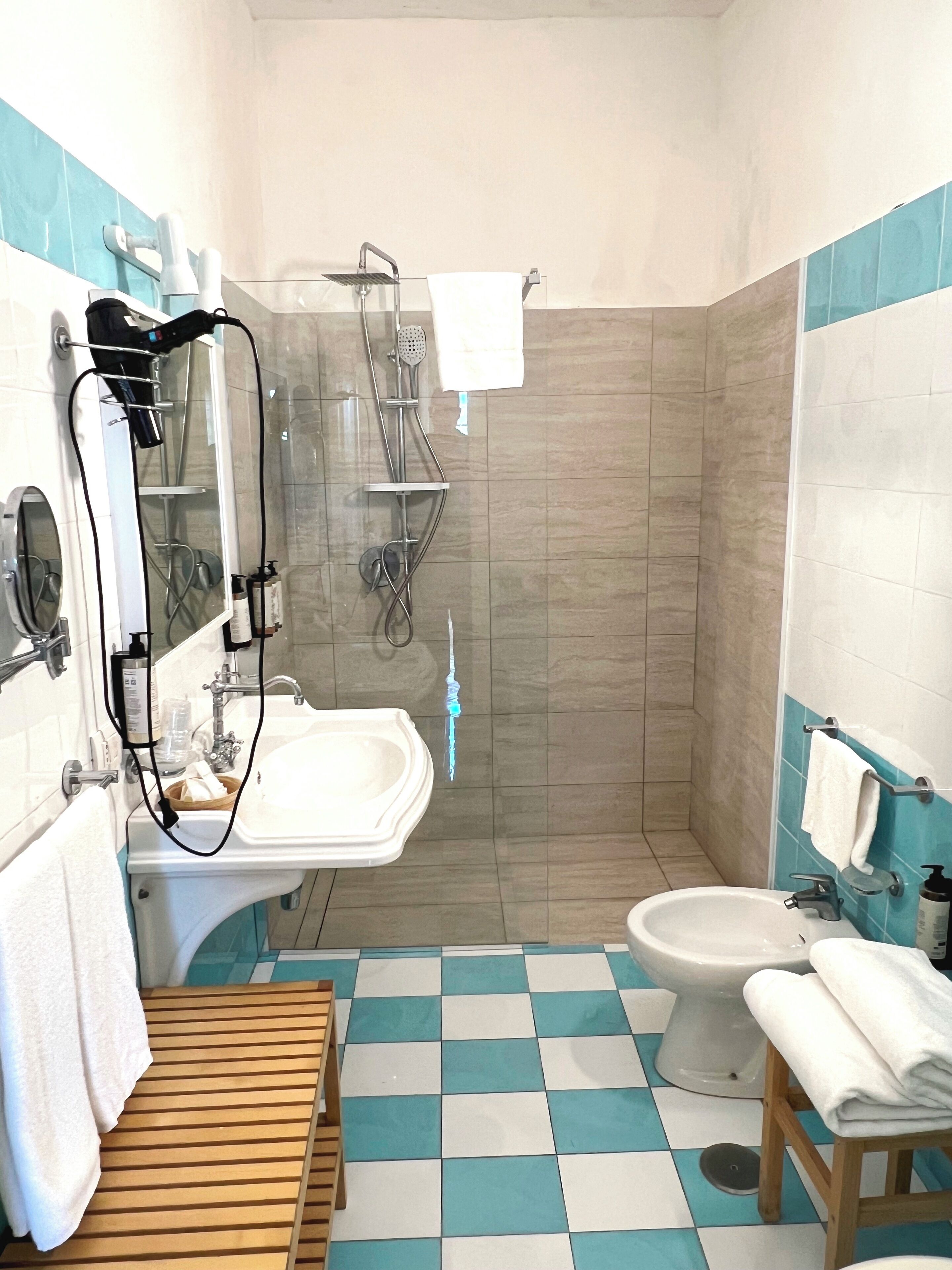 Casa de banho com lavatório, espelho, porta-toalhas, chuveiro e chão xadrez.