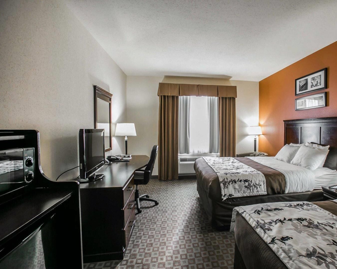 A hotel room with two beds, a desk with a computer, a chair, and a television.