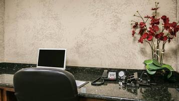 Un escritorio con una computadora portátil, un teléfono y un florero con flores rojas.