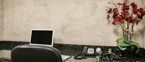 A desk with a laptop, a telephone, and a vase with red flowers.