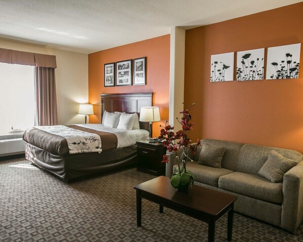 A hotel room with a bed, a sofa, a coffee table, and wall art. - Sleep Inn & Suites Highway 290/NW Freeway (Houston)