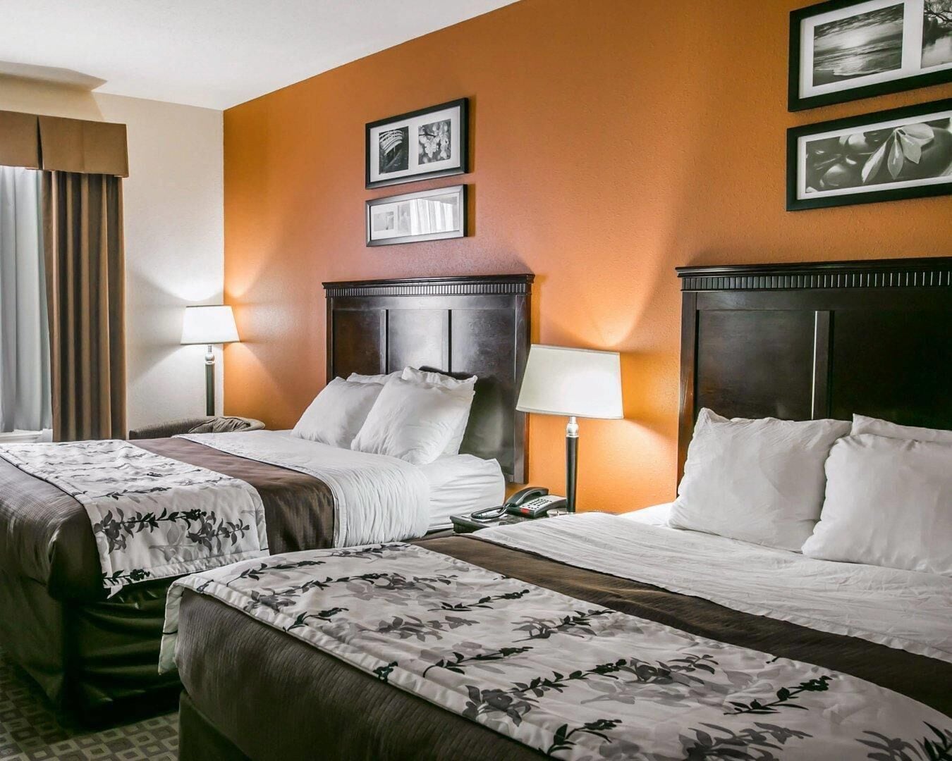 A hotel room with two beds, each with a headboard, bedside lamps, and a telephone on the nightstand.