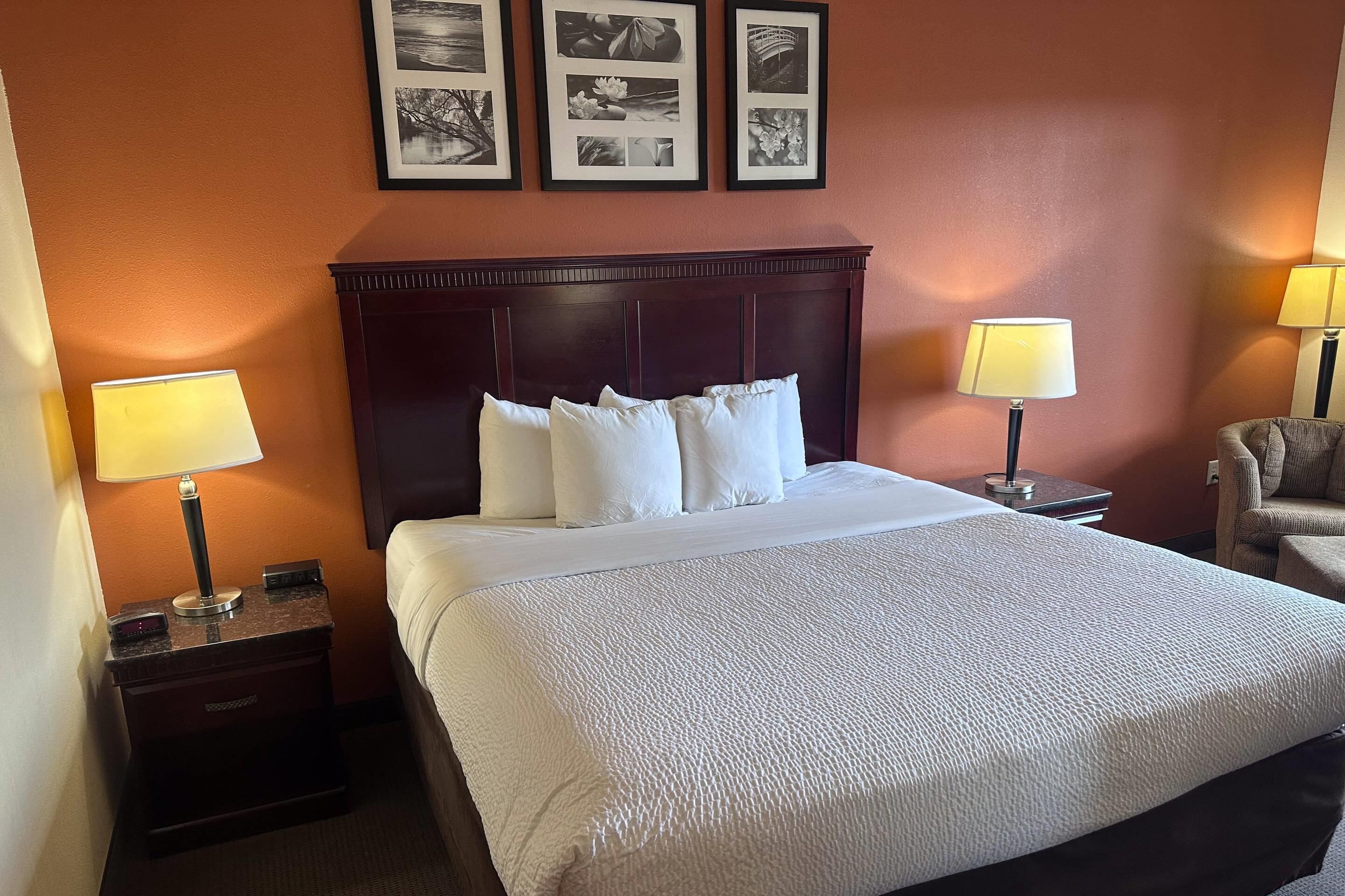 A hotel room with a large bed, two bedside tables with lamps, a chair, and a wall with three framed pictures.