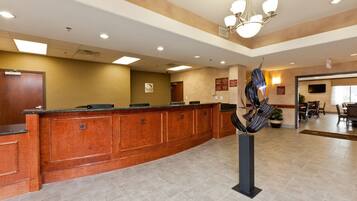 A hotel reception area with a wooden reception desk, a chandelier, and a seating area with tables and chairs.