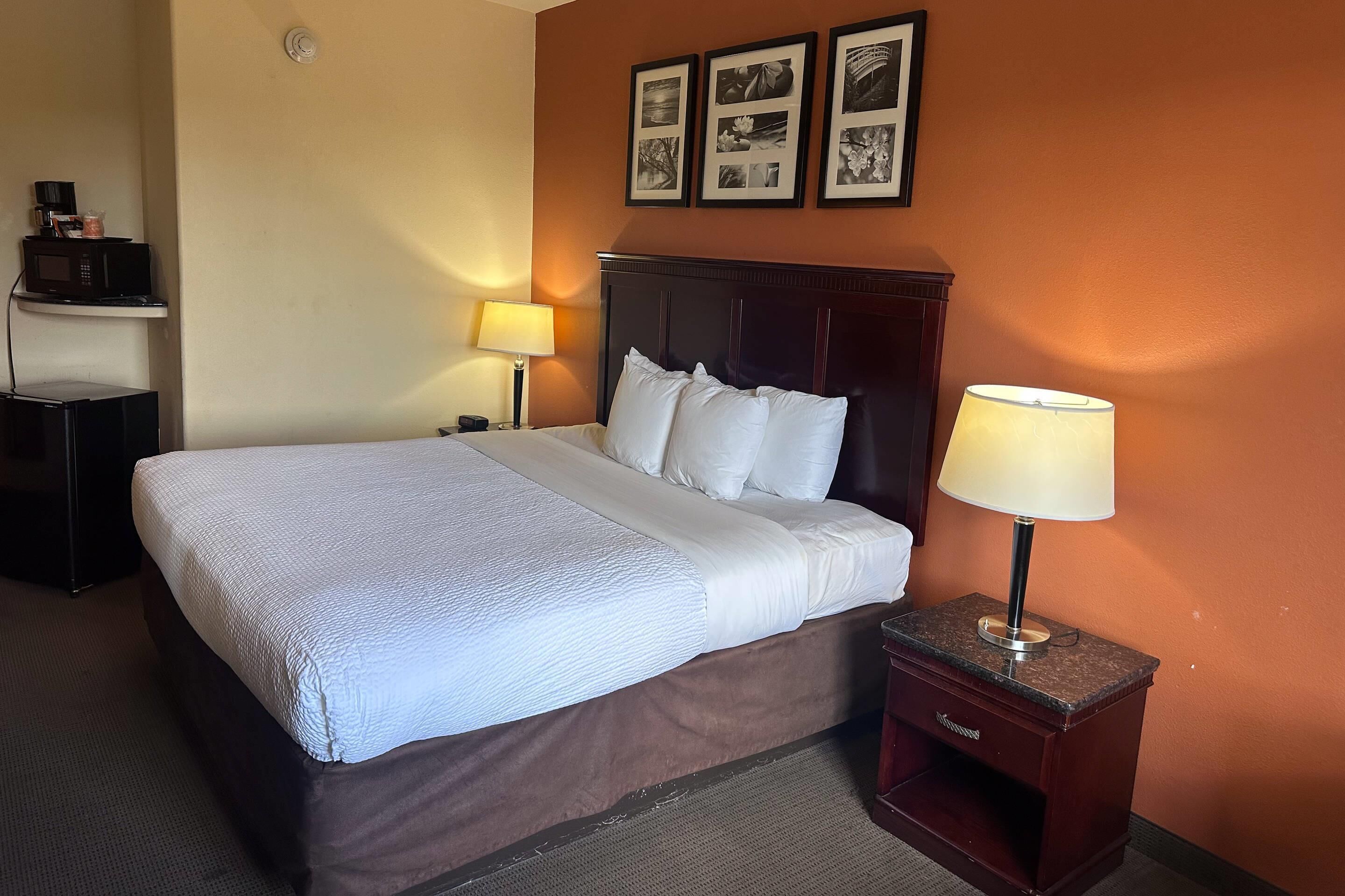 A hotel room with a bed, two bedside tables, a lamp, and a wall-mounted picture frame.