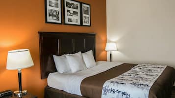 Habitación de hotel con una cama grande, dos lámparas de noche, una mesita de noche y una pared con tres cuadros.