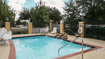 A swimming pool with a tiled edge, a metal ladder, and a few lounge chairs.