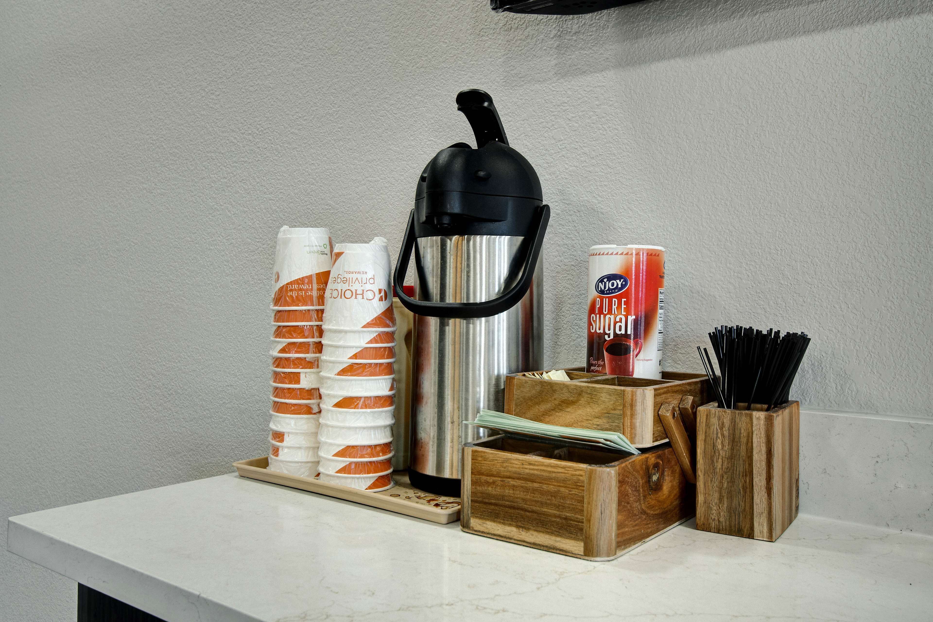 Een keukentafel met een waterkoker, een suikerbus, een bakje room en een houten keukengerei houder.