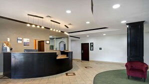 A reception area with a curved desk, a red chair, and a patterned rug. - Motel 6 Fort Worth, TX – I-35 & I-20   (Fort Worth)