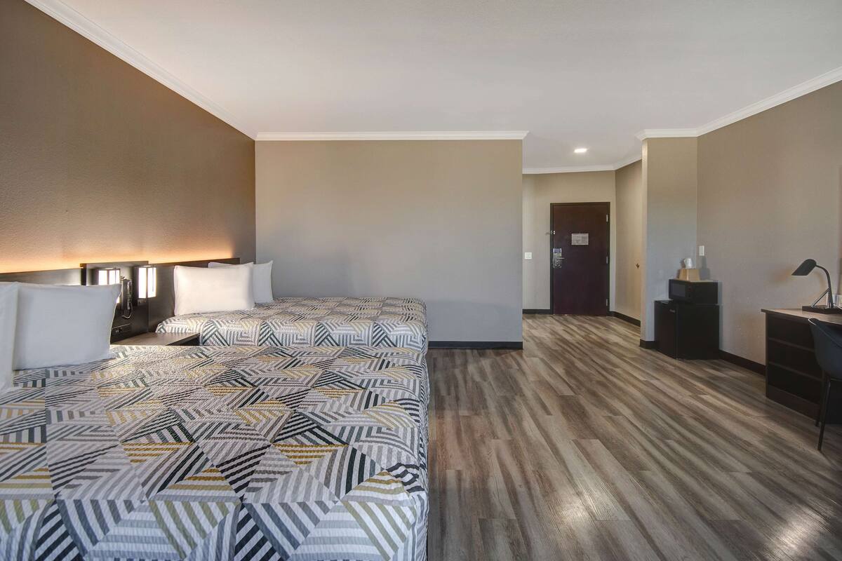 A hotel room with two beds, a desk, and a chair.