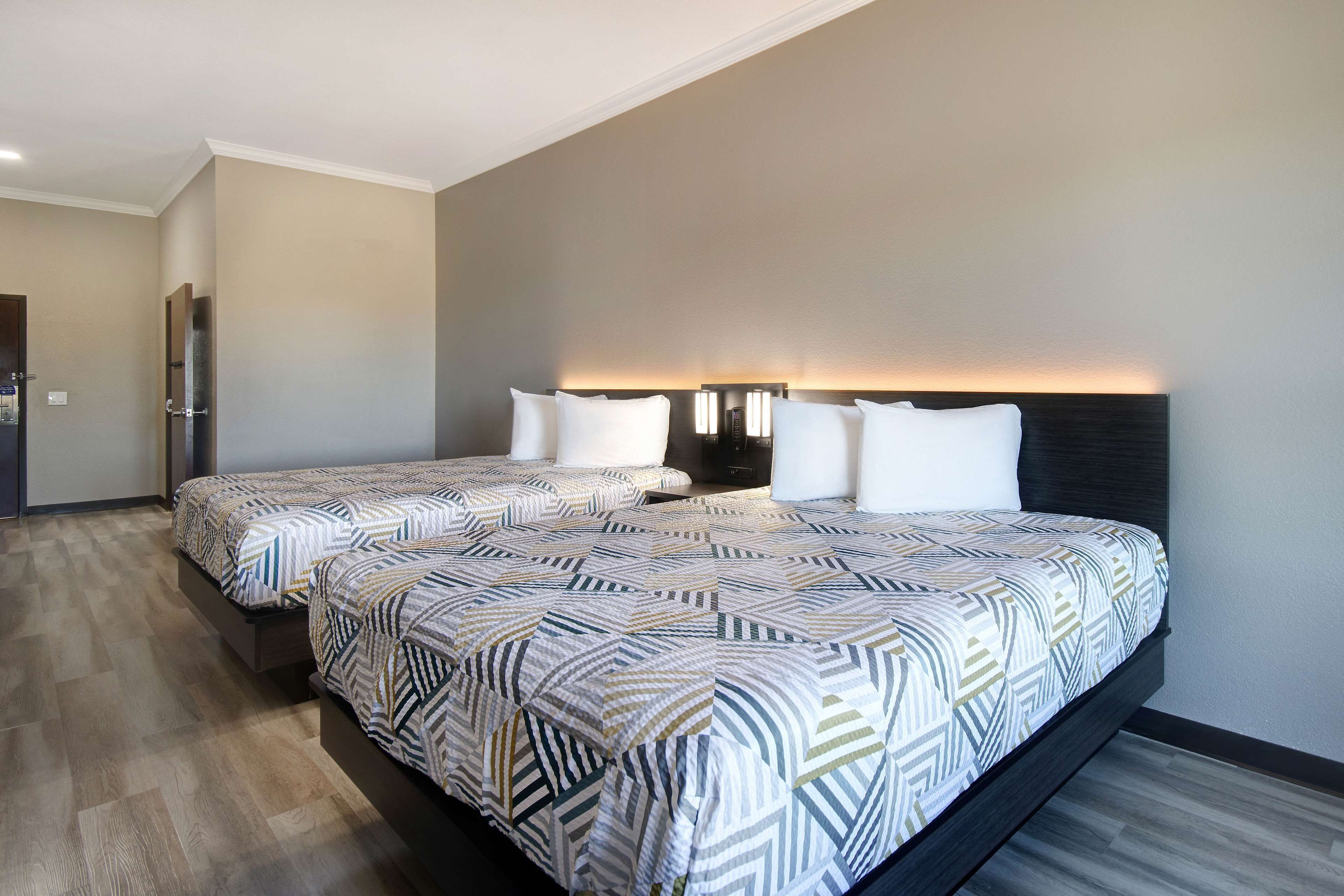 A hotel room with two beds, a dark headboard, and a wall-mounted light fixture.