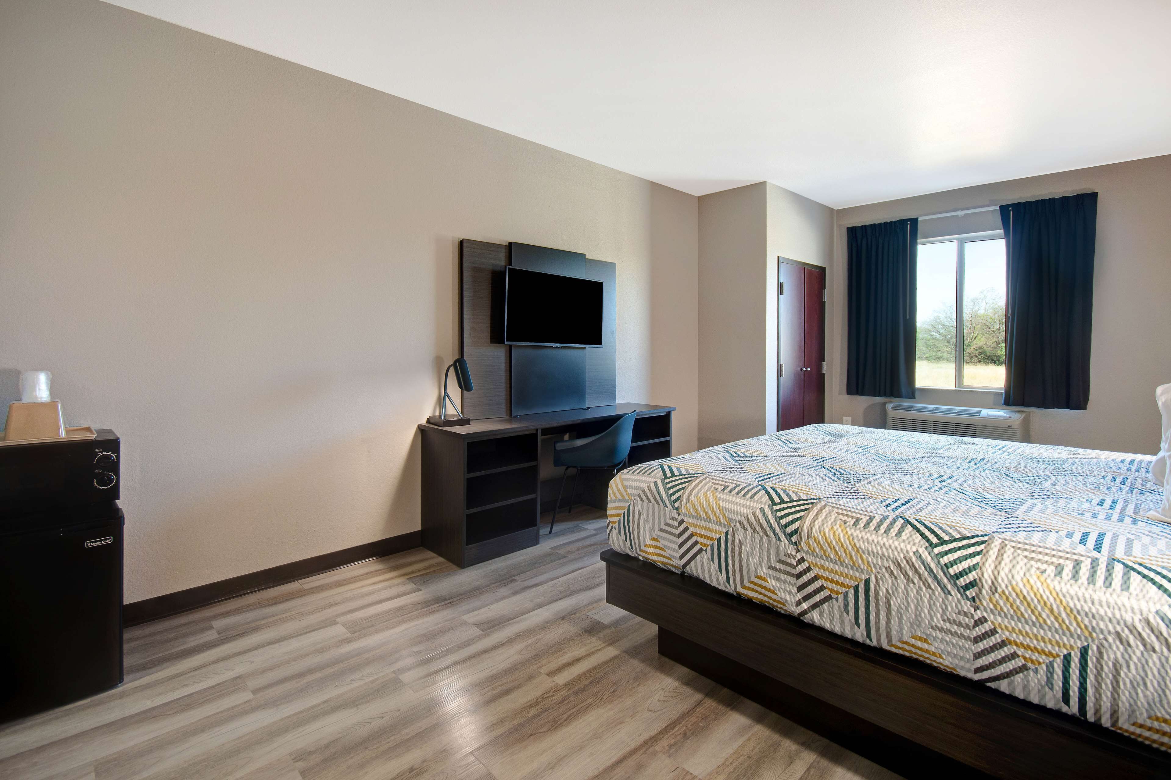 Ein Hotelzimmer mit Bett, Wandfernseher, Schreibtisch mit Stuhl und Kleiderschrank.