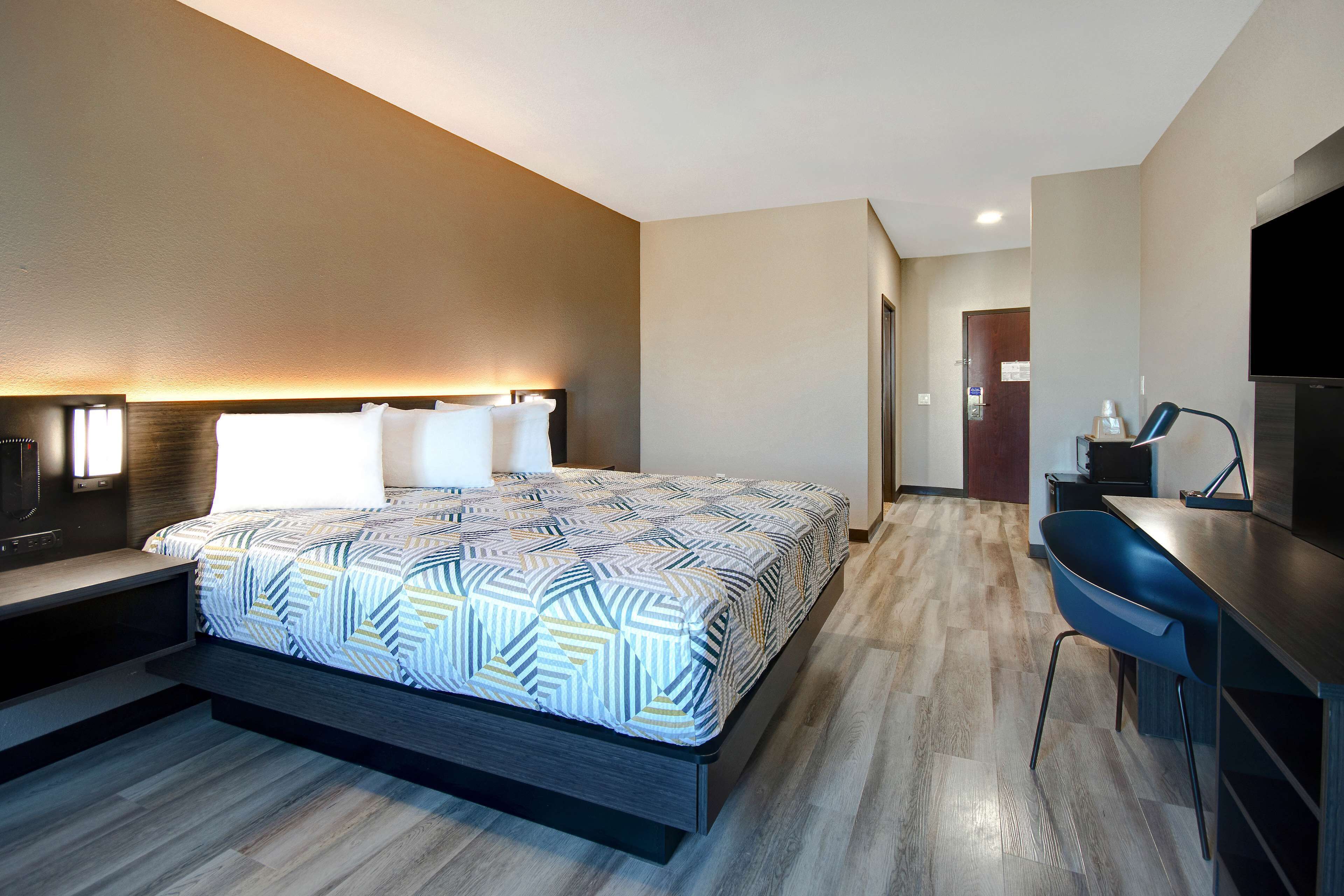 A modern hotel room with a large bed, a desk with a chair, a flat-screen TV, and a nightstand.