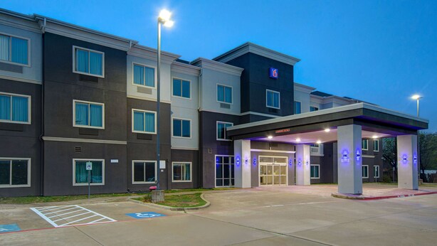 A modern hotel entrance with a covered waiting area, handicap accessible parking, and a clear sky. - Motel 6 Fort Worth, TX – I-35 & I-20   (Fort Worth)