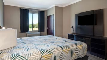A hotel room with a large bed, a flat-screen TV mounted on the wall, a desk with a chair, and a window with curtains.