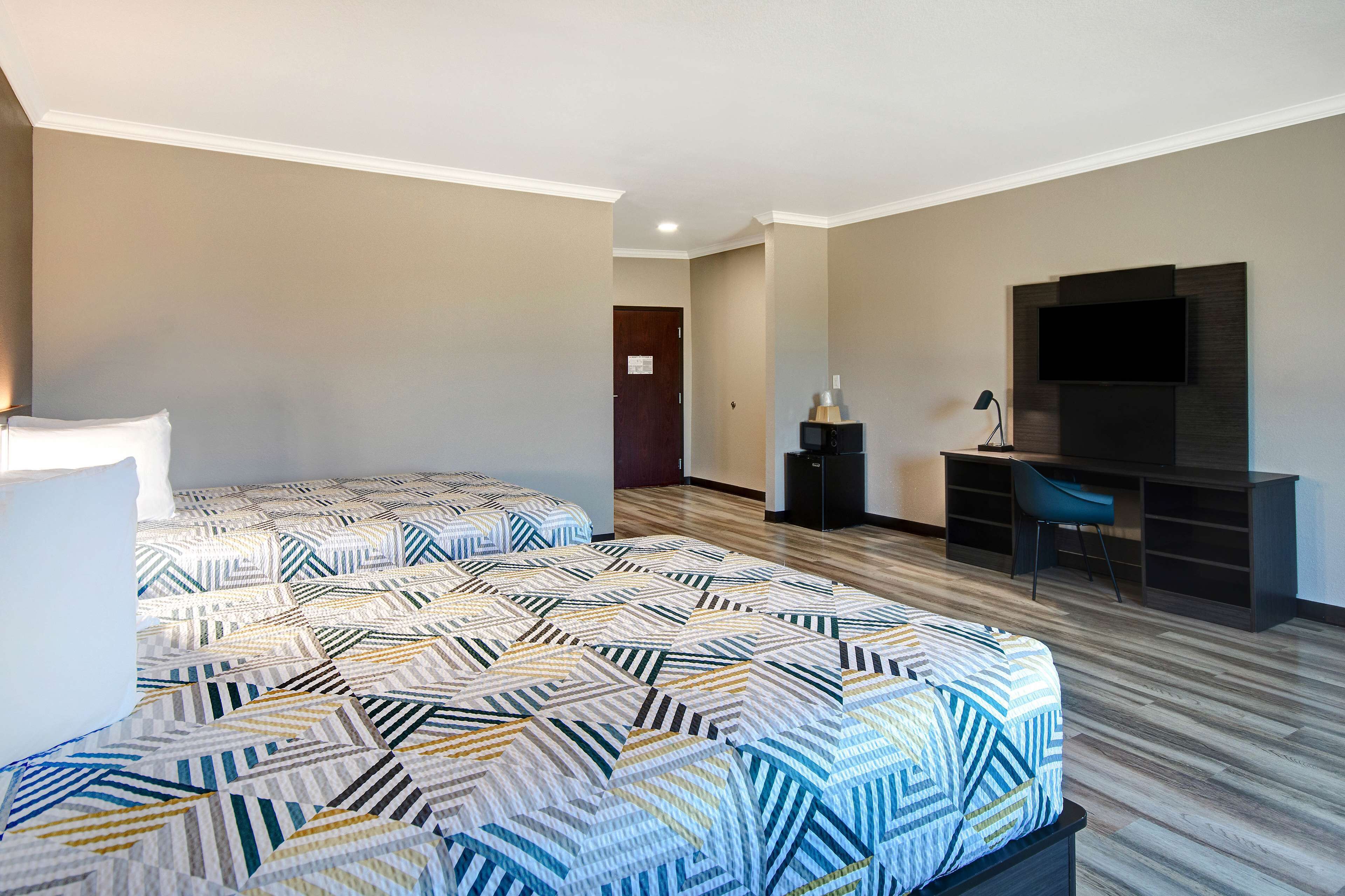 A hotel room with two beds, a desk, a chair, a TV, and a door.