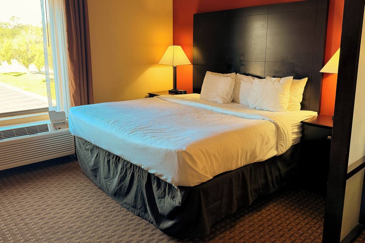 A hotel room with a large bed, two bedside lamps, a window with curtains, and a wall heater.