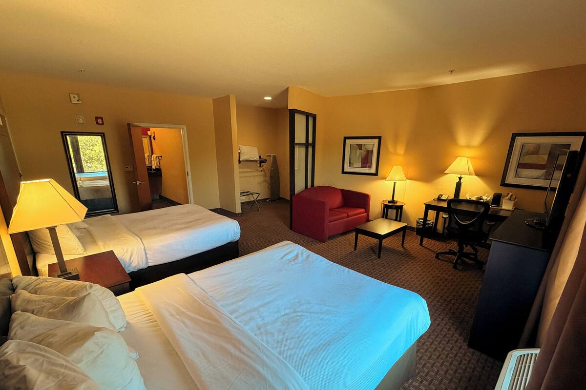 A hotel room with two single beds, a red sofa, a desk with a chair, and a small table.
